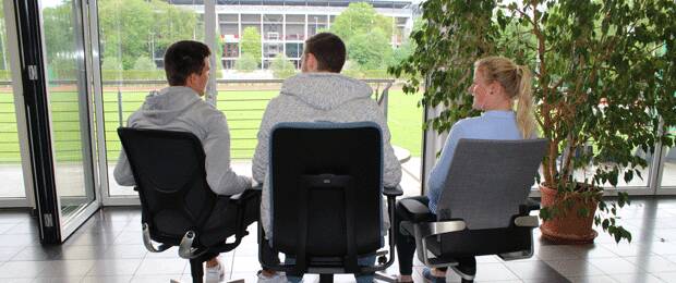 Studenten der Sporthochschule Köln testen die Bürostühle von Wilkhahn. Im Hintergrund erkennt man das Rhein Energie Stadion.